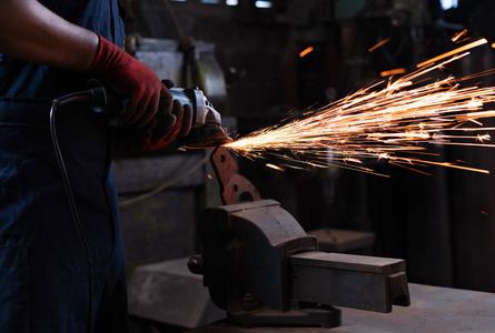 黑金属车间用热火花操作角磨机刀具-工业工人的手在生产工厂炼铁照片
